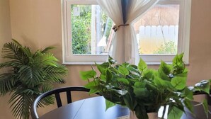 Uma mesa de jantar com um descanso de tecido trançado, um vaso de planta e uma janela com cortinas leves.