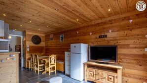Een houten interieur met een eethoek, een koelkast, een televisie en een klok.