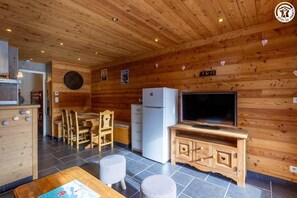 Ein Holzinnenraum mit Essbereich, einem Kühlschrank, einem Fernseher und einer Uhr.
