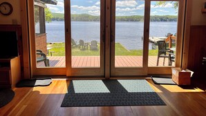 A room with a wooden floor, a television, and a view of a lake through glass doors. - 4th Lake Getaway, Screened Porch, Large Deck & Private Dock (Old Forge)