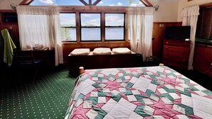 A bedroom with a large window, a bed with a quilt, a chair, a dresser, and a television. - 4th Lake Getaway, Screened Porch, Large Deck & Private Dock (Old Forge)