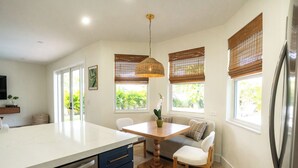 A modern kitchen with a central island, wooden chairs, a dining table, and a hanging light fixture. - NEW Luxe Wellness Retreat - Private Gym, Pilates, Sauna, Pool (Delray Beach)