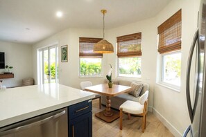 A modern kitchen with a central island, wooden chairs, a dining table, and a hanging light fixture.