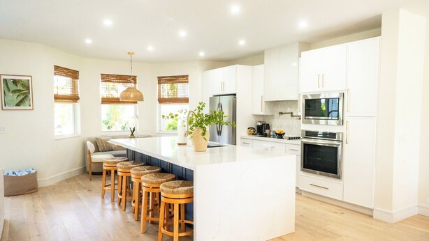 A modern kitchen with a central island, wooden bar stools, white cabinetry, and stainless steel appliances. - NEW Luxe Wellness Retreat - Private Gym, Pilates, Sauna, Pool (Delray Beach)