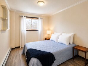 Een slaapkamer met een bed, een bedlamp, een raam met gordijnen en een houten vloer.