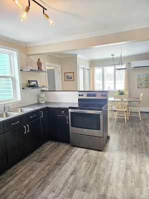 A kitchen with a central island, a stove, and a dining area with chairs.