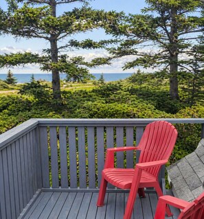 Una silla Adirondack roja sobre una terraza de madera, con vista a árboles y un cuerpo de agua.