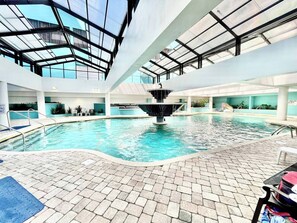 Une piscine intérieure dotée d’une fontaine centrale, entourée d’un sol carrelé et surmontée d’un plafond en verre.