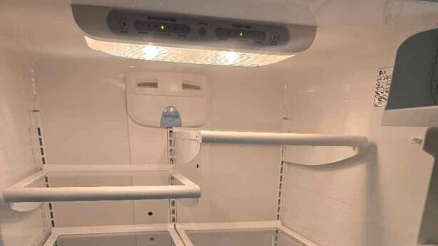 Un refrigerador vacío con repisas y dispensador de agua.