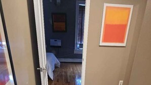 Un pasillo con piso de madera que lleva a un dormitorio con cama y ventana.