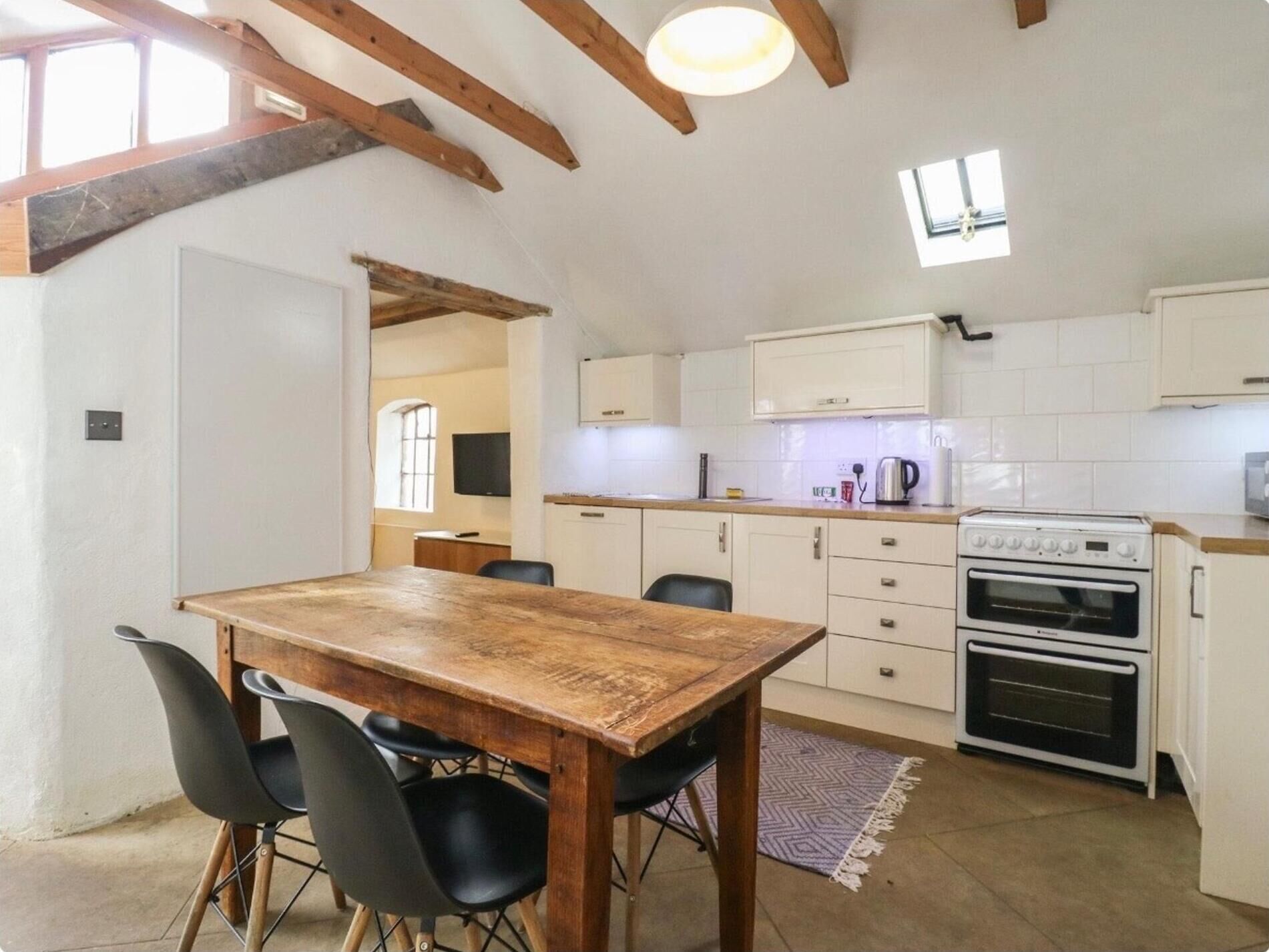 A kitchen with white cabinets, a wooden table, and black chairs.