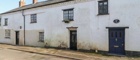 A white building with a blue door, a sign reading "The Root," and a small window with a plant.