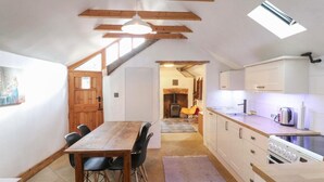 Una cocina compacta con vigas de madera, una mesa de comedor con sillas y una estufa pequeña.