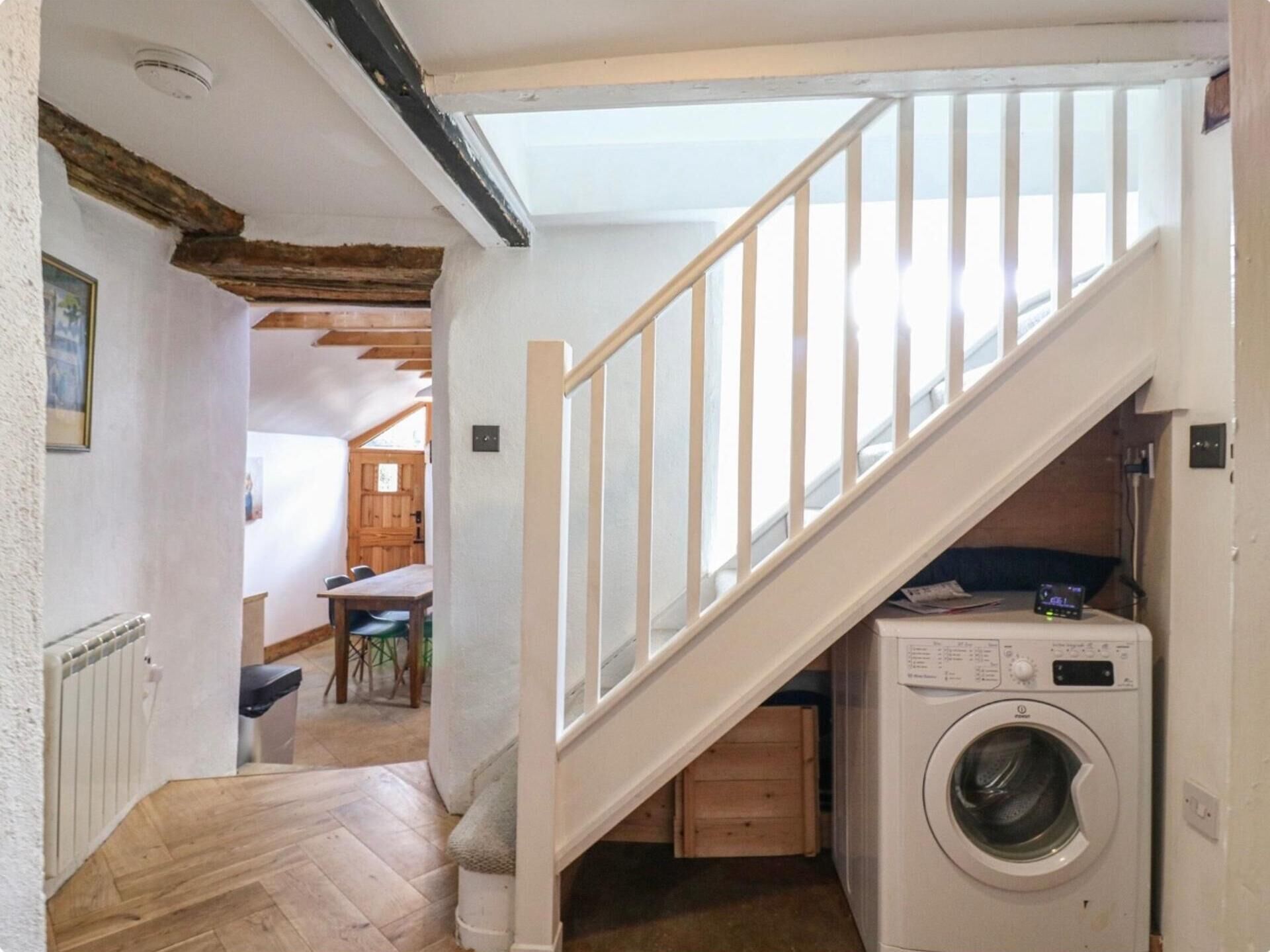 Un espace buanderie avec un lave-linge, un escalier en bois et, au fond, un coin repas.