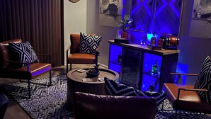 Ett modernt vardagsrum med en soffa, fåtöljer, ett soffbord och en bardisk med flaskor och en dekorativ detalj.