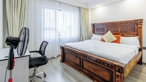 Ein Hotelzimmer mit einem Holzbett, einem Schreibtisch mit Stuhl und einem Standventilator.