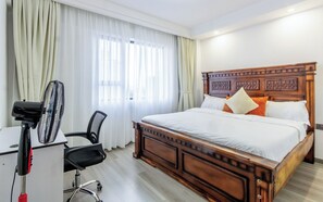 Ein Hotelzimmer mit einem Holzbett, einem Schreibtisch mit Stuhl und einem Standventilator.