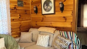 Interno di una baita di legno con un divano, cuscini, un quadro incorniciato e applique a parete.