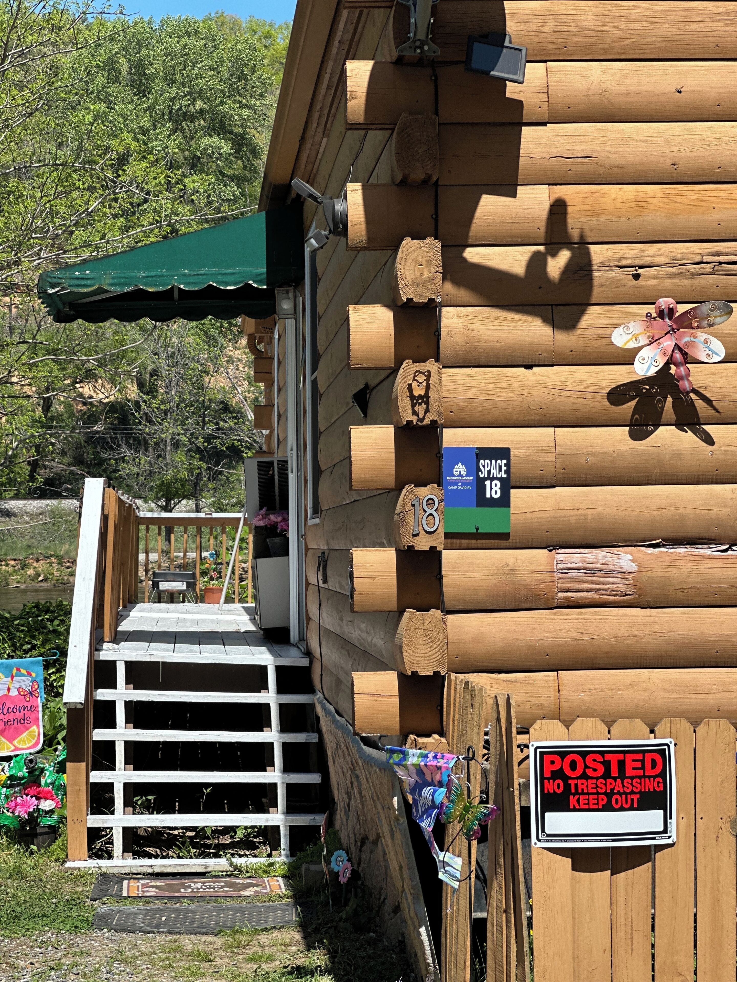 A wooden cabin with a porch, a 'SPACE 18' sign, and a 'POSTED NO TRESPASSING KEEP OUT' sign.