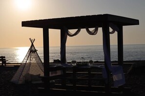 A beach scene with a wooden gazebo, a teepee, and a table set for a meal. - Harbor Heritage House | Lake Views & Sunset Deck (Conneaut)