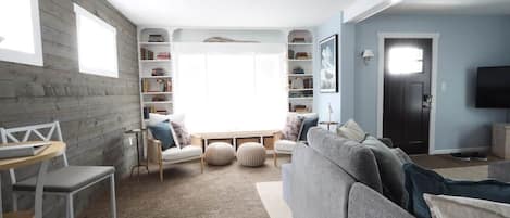 Un salón con un sofá gris, una silla blanca, una mesita y una estantería.