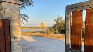 An open gate leading to a gravel path with a view of a tower-like structure in the distance. - Fronte Mare 2 (Torre Lapillo)