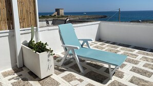 A balcony with a white railing, a blue lounge chair, and a potted plant. - Fronte Mare 2 (Torre Lapillo)
