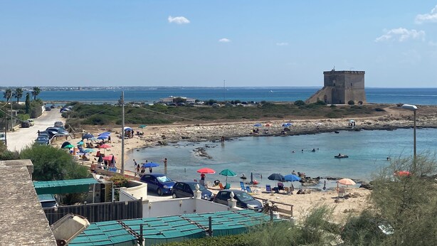 A coastal area with a beach, a tower, parked cars, and umbrellas. - Fronte Mare 2 (Torre Lapillo)
