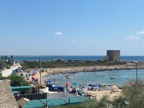 Une zone côtière avec une plage, une tour, des voitures garées et des parasols.