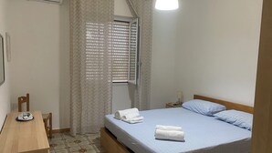 A bedroom with a bed, a desk, a chair, a window with blinds, and a hanging light fixture. - Fronte Mare 2 (Torre Lapillo)
