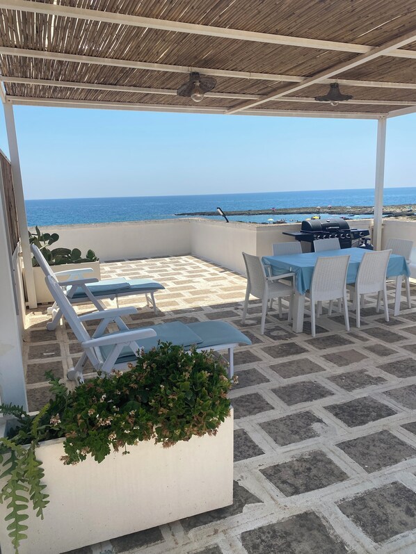 Un espace extérieur abrité, aménagé avec des sièges, et offrant une vue sur la plage et l’océan.