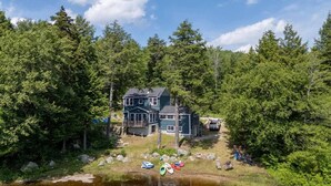 A two-story house with a dock extending into a lake, surrounded by dense forest. - Waterfront Family Getaway with Sunroom & Stunning Views (Washington)