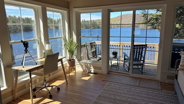 A room with large windows overlooking a lake, a telescope, a desk, and a cozy seating area with a view. - Waterfront Family Getaway with Sunroom & Stunning Views (Washington)