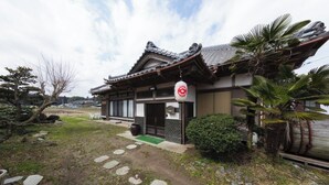 Ein traditionelles japanisches Gebäude mit einem Ziegeldach, einem kleinen Garten mit trittfesten Steinen und einem Schild, das auf ein Restaurant oder ein Café hinweist.