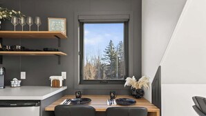 A compact kitchen with a window, a dining table set for two, and a dishwasher. - Osprey Cabin - Ocean Front Acadia A Frame Cabin (Tremont)