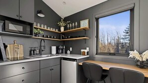 A modern kitchen with grey cabinets, a built-in microwave, and a window with a view of trees. - Osprey Cabin - Ocean Front Acadia A Frame Cabin (Tremont)