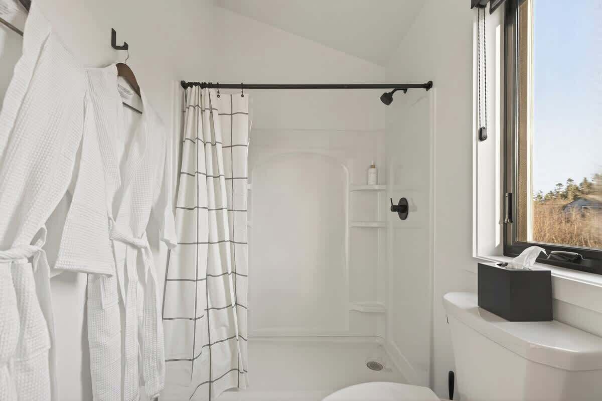 Een badkamer met een douche, toilet, raam en een handdoekrek met witte handdoeken.