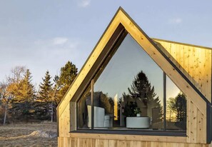 A modern wooden cabin with a triangular roof, large windows, and a visible interior with a white chair and a round table. - Evergreen Cabin Ocean Front Acadia A Frame Studio (Tremont)