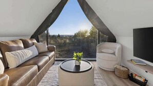 A modern living room with a large window, a sofa, a chair, a coffee table, and a flat-screen TV. - Evergreen Cabin Ocean Front Acadia A Frame Studio (Tremont)
