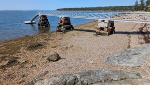 A rocky shoreline with a bridge, a wooden dock, and a distant forested island. - Evergreen Cabin Ocean Front Acadia A Frame Studio (Tremont)