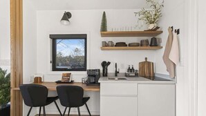 A compact kitchen with a window, two black chairs, a coffee machine, and wooden shelves. - Evergreen Cabin Ocean Front Acadia A Frame Studio (Tremont)