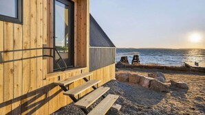 A wooden building with a large window, a staircase, and a view of the sea. - Sunset Oceanfront Cabin with Sauna, Beach and Dock (Tremont)