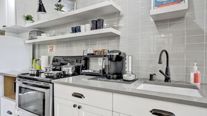 Moderni keittiö, jossa on valkoiset kaapit, sisäänrakennettu uuni, kahvinvalmistusalue ja hana, jossa on pesuallas.