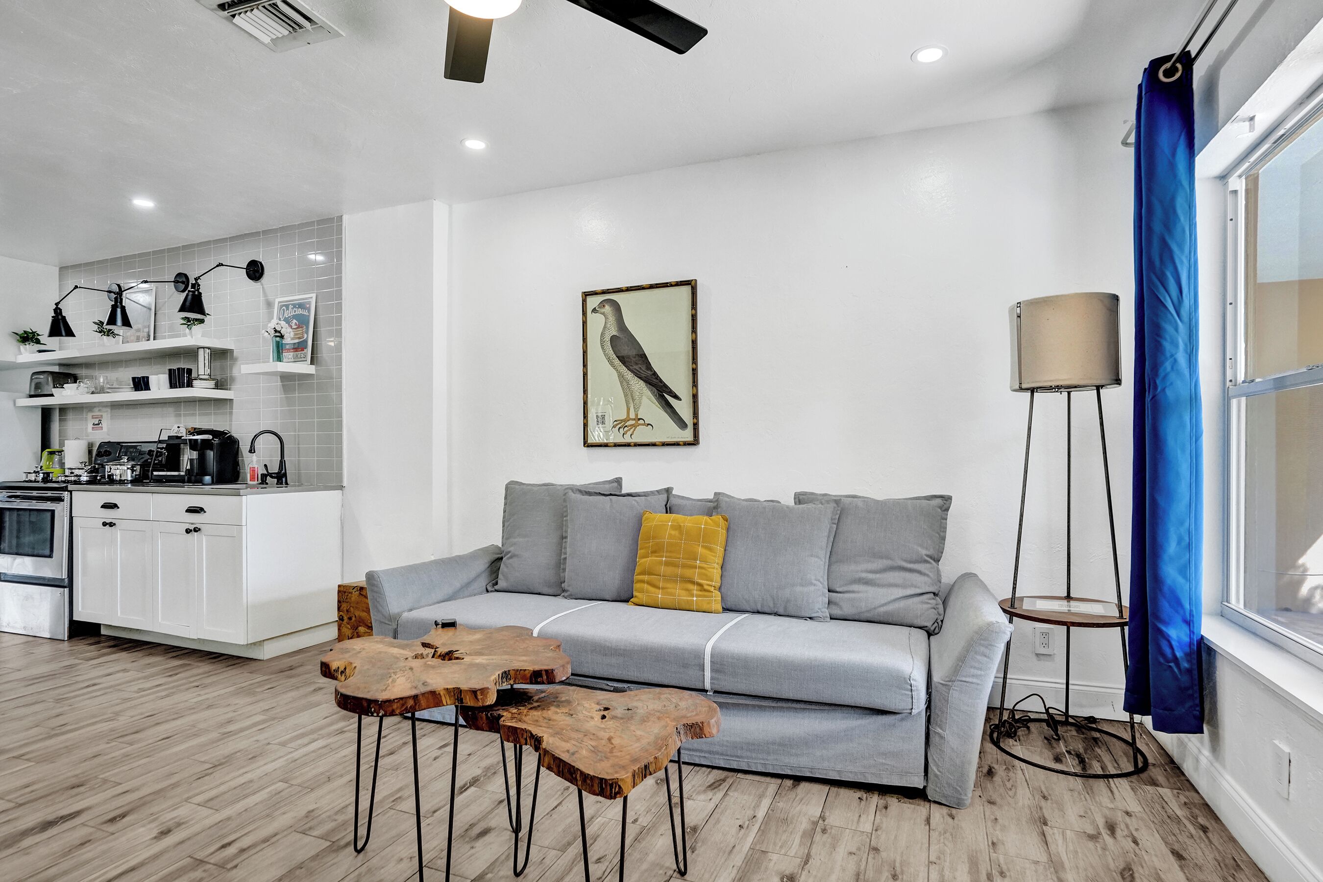 A modern living room with a grey sofa, wooden coffee table, and a painting of a bird on the wall.