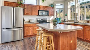 A modern kitchen with wooden cabinets, stainless steel appliances, and a large island with stools. - Nature Art Retreat on Breckenridge Creek w/ Pond! (Sumas)