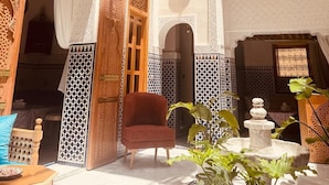 Pátio interno com trabalhos em azulejos detalhados, uma cadeira de madeira e uma fonte.