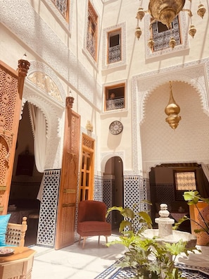 An interior courtyard with intricate tile work, a wooden chair, and a fountain. - Dar Magic Fes (Fes)