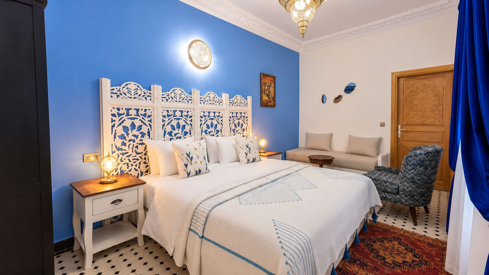 A bedroom with a bed, nightstands, a chair, a sofa, a patterned rug, and a decorative wall panel.