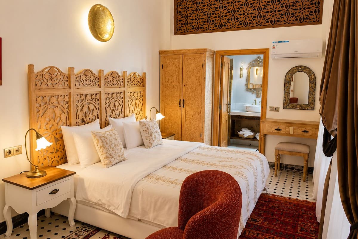 A hotel room with a bed, bedside tables, a mirror, a wardrobe, and a bathroom visible through an open door.