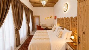 A hotel room with a large bed, a wooden headboard, a small seating area, and a decorative wall panel. - Dar Magic Fes (Fes)